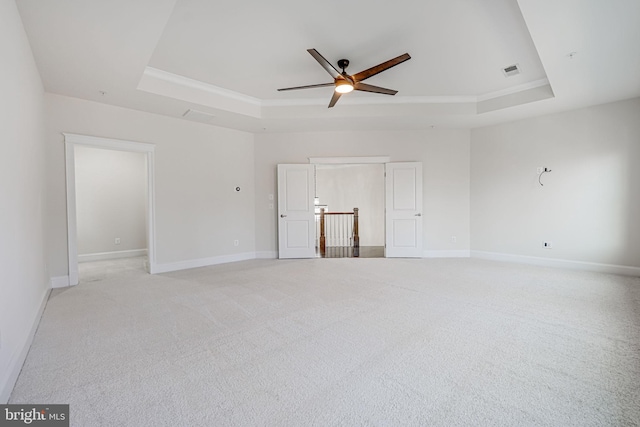 spare room with a raised ceiling, ceiling fan, light colored carpet, baseboards, and ornamental molding