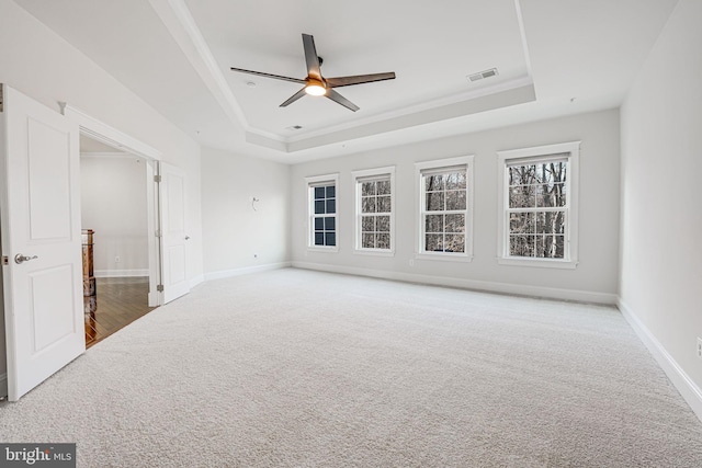 unfurnished room with a raised ceiling, carpet, ceiling fan, crown molding, and baseboards