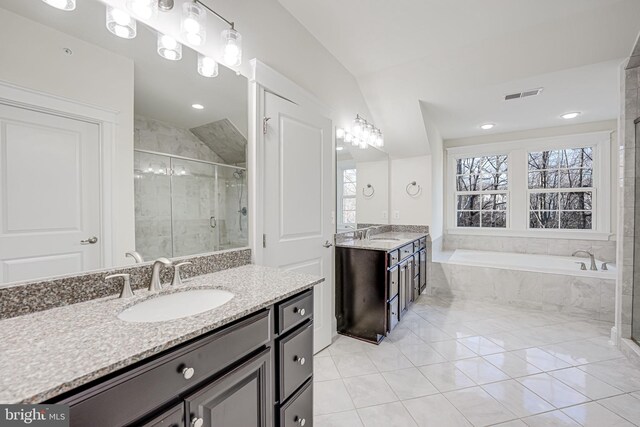 full bathroom featuring a stall shower, a bath, vaulted ceiling, two vanities, and tile patterned floors
