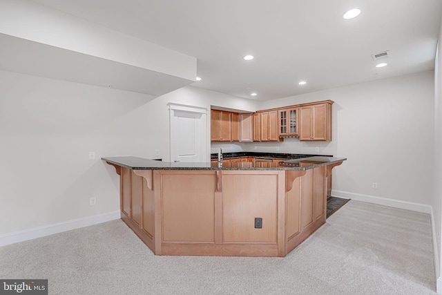 kitchen with a breakfast bar, dark stone countertops, light colored carpet, glass insert cabinets, and baseboards