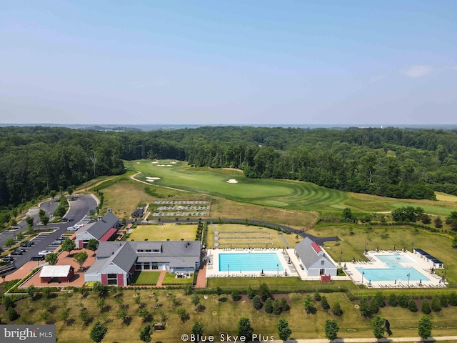 drone / aerial view of a pool, a heavily wooded area, and a local golf course