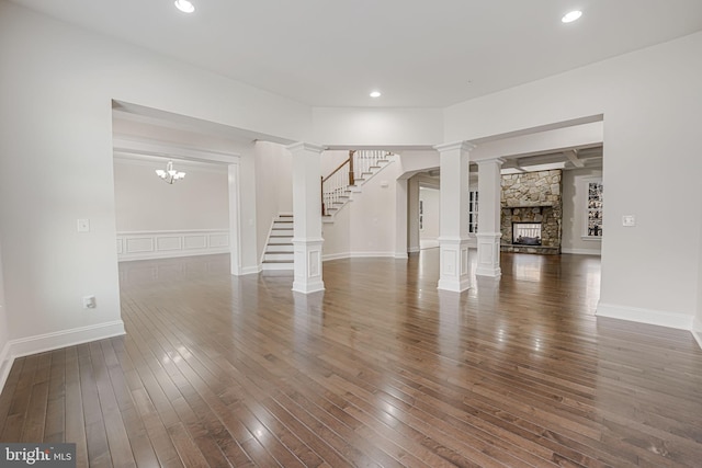 unfurnished living room with dark wood-style floors, a stone fireplace, stairway, decorative columns, and recessed lighting