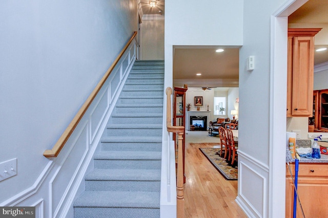 staircase featuring a decorative wall, wood finished floors, a glass covered fireplace, recessed lighting, and a wainscoted wall