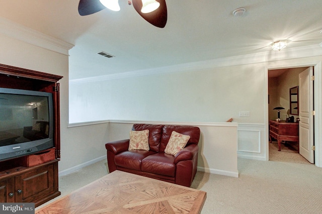 living area with a ceiling fan, crown molding, light carpet, and a wainscoted wall