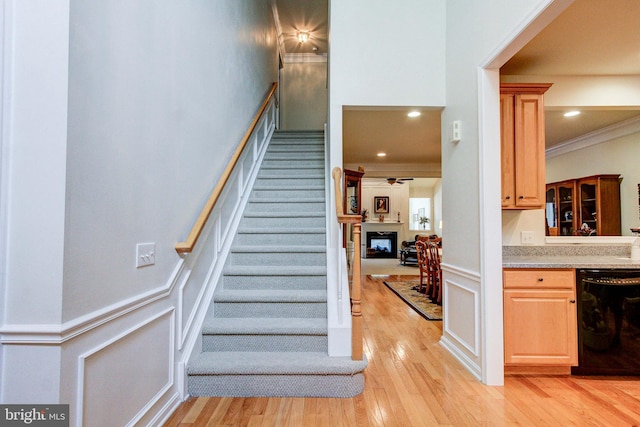 stairs featuring a decorative wall, wood finished floors, a wainscoted wall, ornamental molding, and a ceiling fan