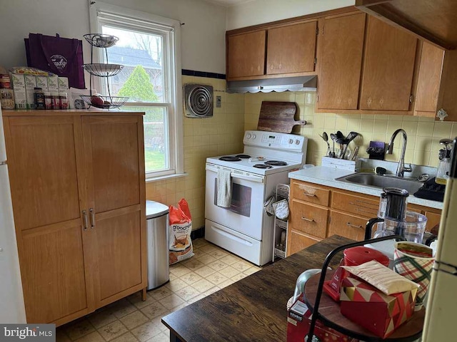 kitchen with electric range, exhaust hood, plenty of natural light, a sink, and tile walls