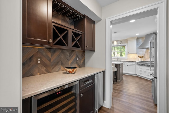 410 Metropolitan Blvd, Pasadena, MD 21122 - indoor dry bar with wall chimney exhaust hood, wine cooler, appliances with stainless steel finishes, decorative backsplash, and wood finished floors