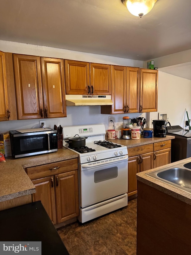kitchen with white range with gas stovetop, stainless steel microwave, under cabinet range hood, a sink, and brown cabinetry