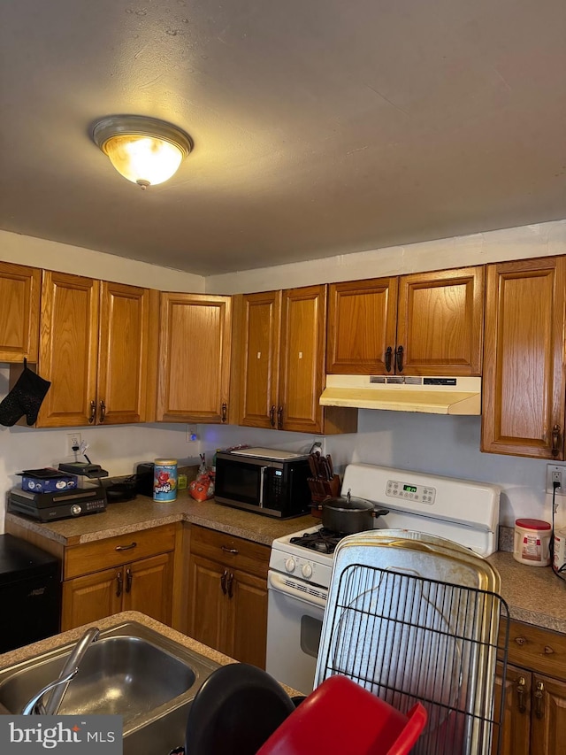 kitchen featuring under cabinet range hood, white gas stove, brown cabinetry, and a sink