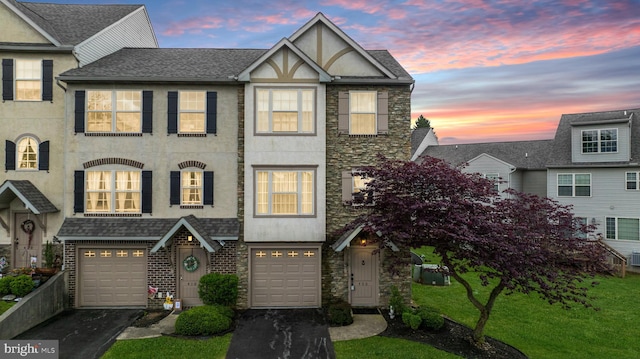 view of property with a garage, stucco siding, driveway, stone siding, and a front lawn