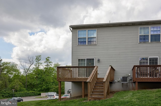 back of property with a deck, stairway, cooling unit, and a lawn