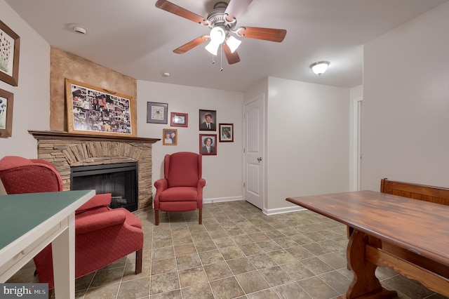 sitting room featuring a stone fireplace, a ceiling fan, and baseboards