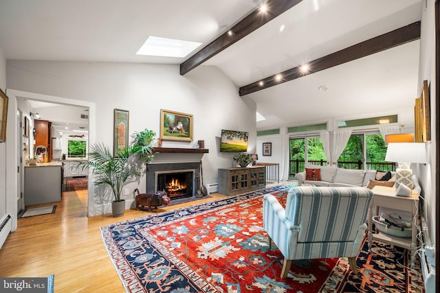 living room with a skylight, light wood-style floors, a baseboard heating unit, and a lit fireplace
