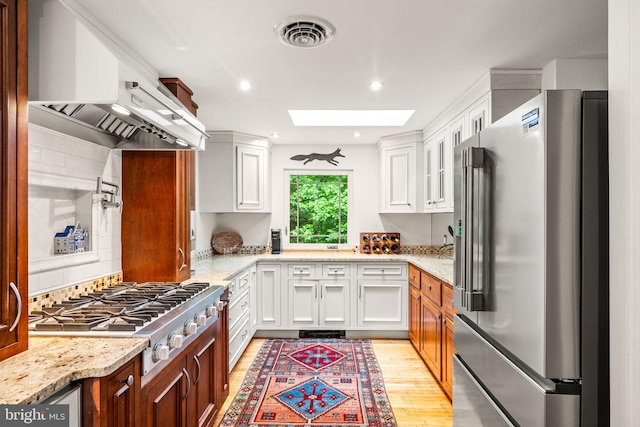 kitchen with appliances with stainless steel finishes, a skylight, light wood-type flooring, white cabinetry, and recessed lighting