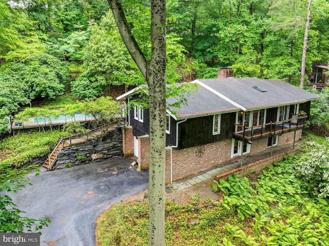 view of side of property featuring a shingled roof, a chimney, stairway, driveway, and brick siding