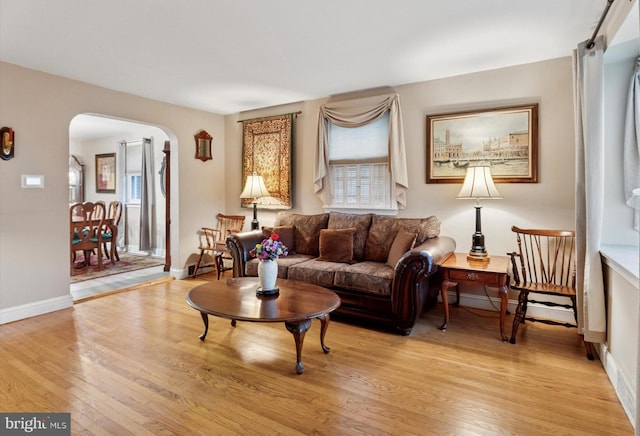 living room featuring arched walkways, light wood-style flooring, and plenty of natural light