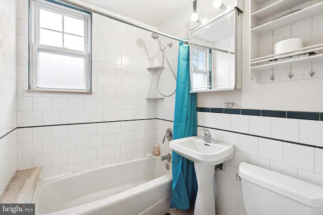 bathroom featuring toilet, shower / tub combo with curtain, healthy amount of natural light, and tile walls