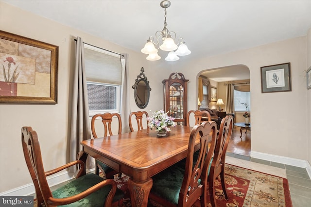 dining space featuring arched walkways, a chandelier, baseboards, and tile patterned flooring