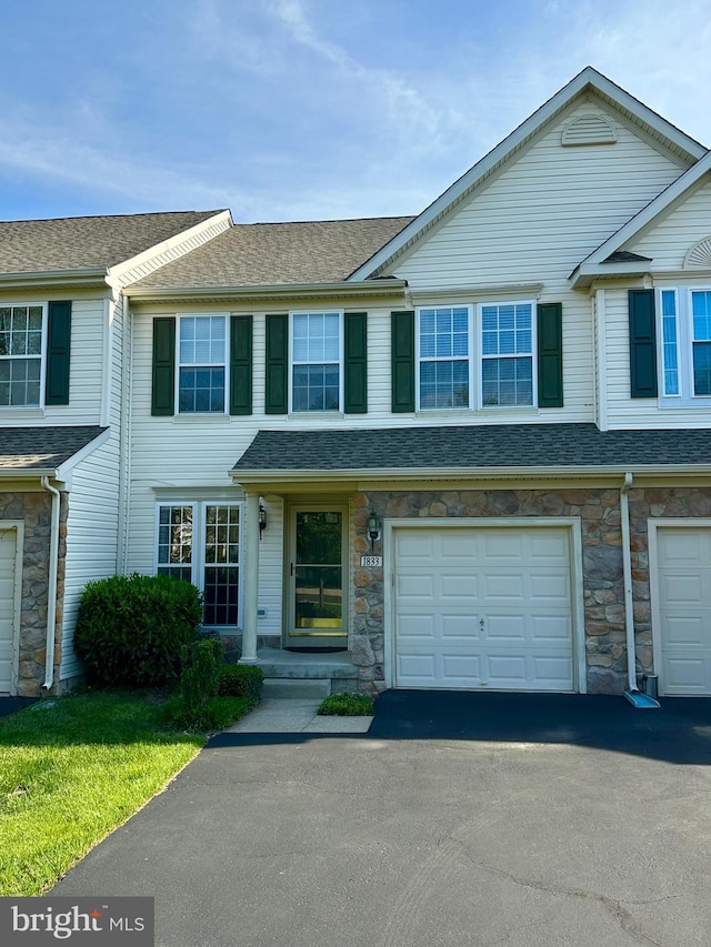 view of property with an attached garage, stone siding, driveway, and roof with shingles