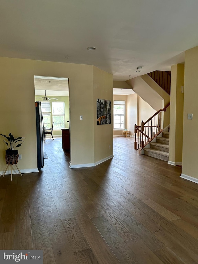 unfurnished living room with plenty of natural light, stairs, baseboards, and dark wood-style floors