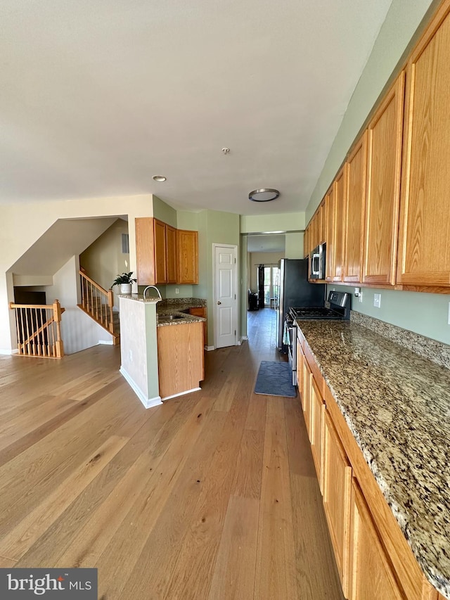 kitchen with appliances with stainless steel finishes, light wood-type flooring, dark stone countertops, recessed lighting, and open floor plan