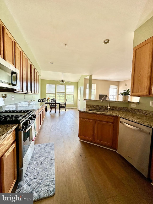 kitchen featuring stainless steel appliances, a sink, brown cabinetry, dark wood-style floors, and recessed lighting