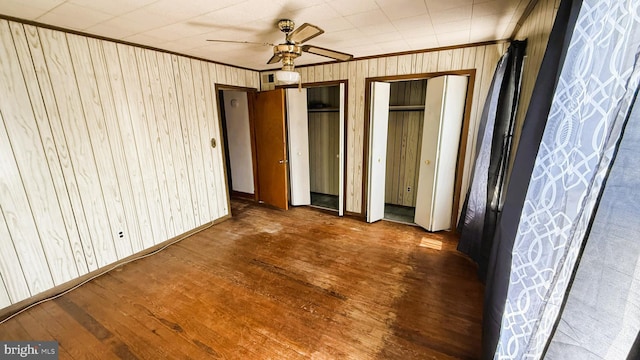 3726 5th St, Baltimore, MD 21225 - unfurnished bedroom with wood finished floors, two closets, crown molding, wooden walls, and ceiling fan