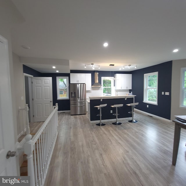 3608 Upshur St, Brentwood, MD 20722 - kitchen featuring stainless steel fridge, wall chimney exhaust hood, white cabinetry, a breakfast bar area, and a center island