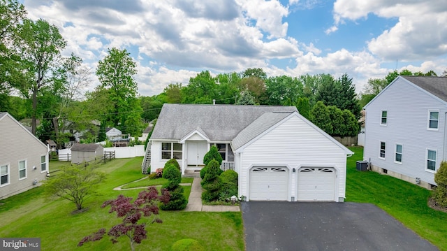 view of front of property with asphalt driveway, an attached garage, a front lawn, roof with shingles, and central AC