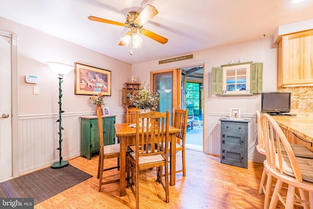 dining area with light wood-style floors, a wainscoted wall, and a ceiling fan