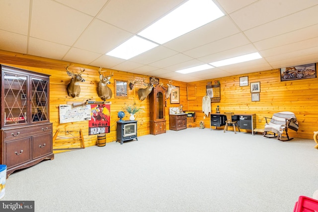 living area featuring carpet floors, a paneled ceiling, a wood stove, and wooden walls
