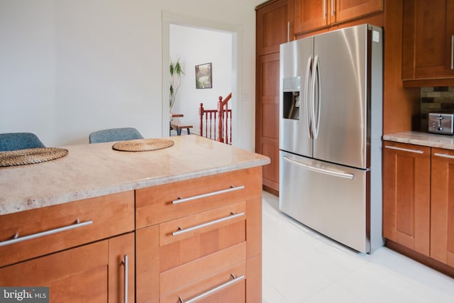 kitchen featuring stainless steel fridge with ice dispenser, brown cabinets, light stone counters, and backsplash