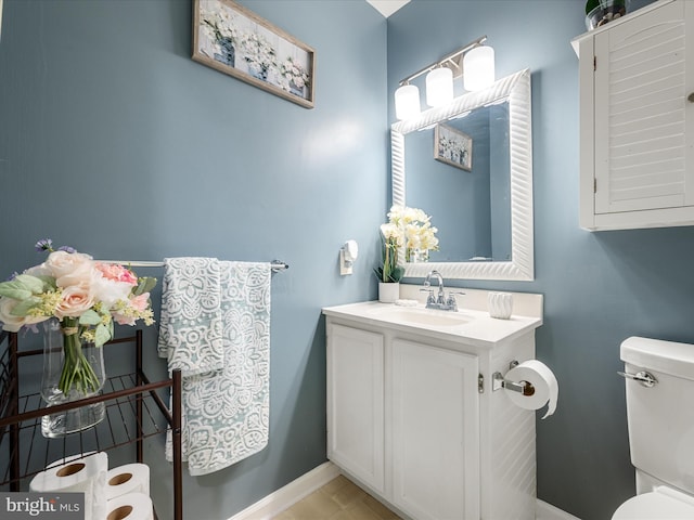 half bathroom featuring toilet, vanity, and baseboards