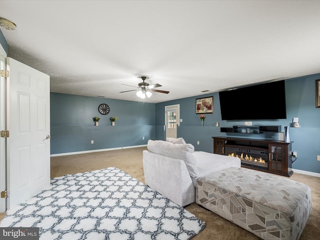 living area featuring carpet, ceiling fan, baseboards, and a warm lit fireplace