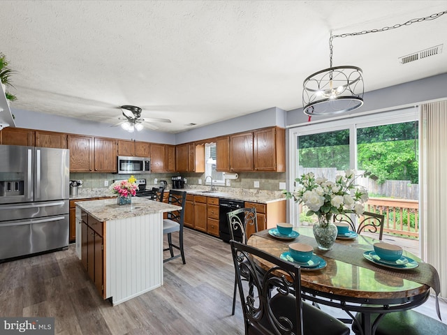kitchen with stainless steel appliances, brown cabinets, a ceiling fan, a center island, and a sink