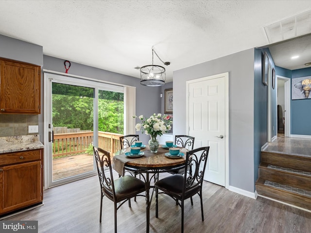dining space featuring light wood-style floors, a chandelier, a textured ceiling, and baseboards