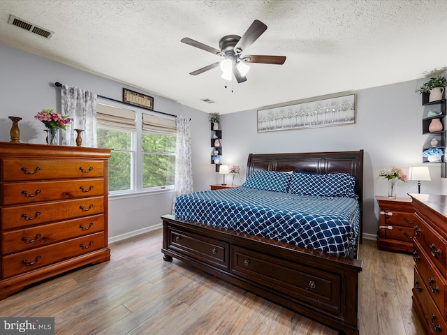 bedroom featuring baseboards, light wood-type flooring, a textured ceiling, and ceiling fan