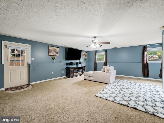 living room with ceiling fan, carpet floors, a textured ceiling, baseboards, and a glass covered fireplace
