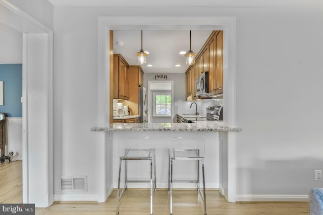 2901 N Rochester St, Arlington, VA 22213 - kitchen with appliances with stainless steel finishes, brown cabinets, light wood finished floors, light stone countertops, and a sink