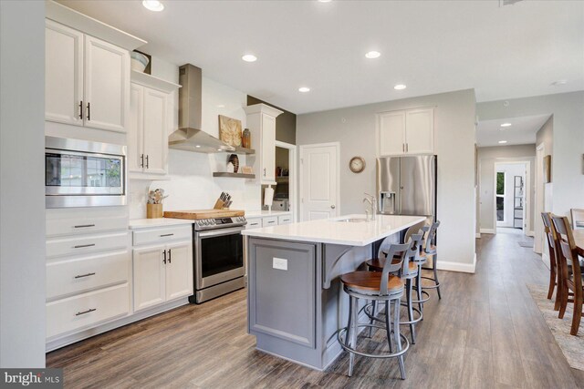 3118 Grove Ct, Mechanicsburg, PA 17055 - kitchen with wall chimney exhaust hood, appliances with stainless steel finishes, dark wood-style floors, a kitchen island with sink, and light countertops