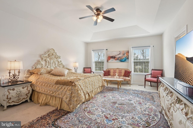 carpeted bedroom featuring a tray ceiling and a ceiling fan