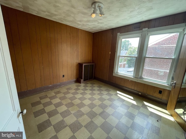 unfurnished room with light flooring, wood walls, a textured ceiling, and baseboards