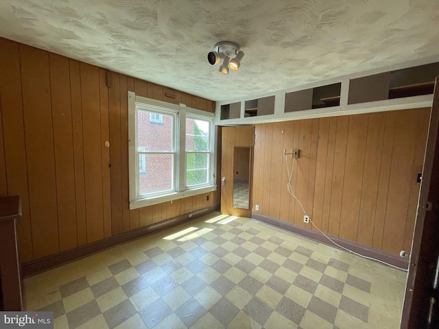 spare room with light floors, wooden walls, a textured ceiling, and baseboards