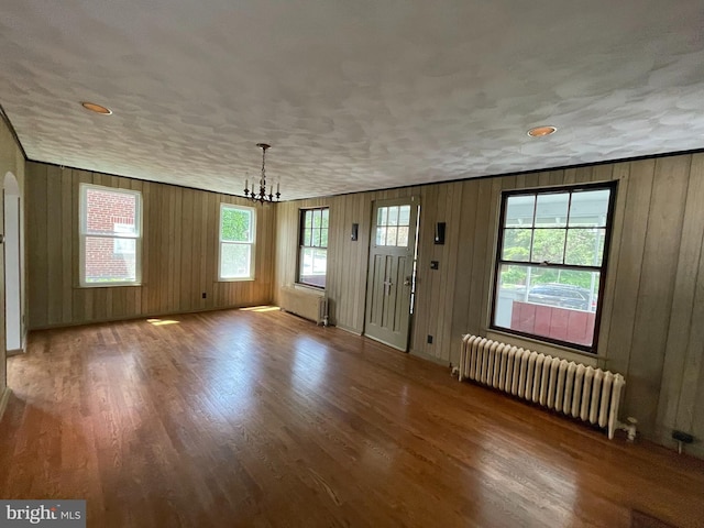 unfurnished dining area with radiator, a chandelier, wood finished floors, arched walkways, and wooden walls