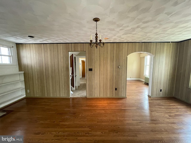 unfurnished dining area with arched walkways, a chandelier, wood finished floors, wooden walls, and radiator heating unit