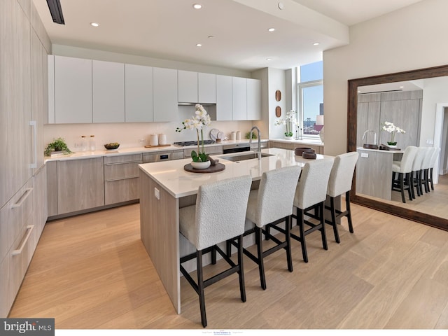 kitchen featuring a sink, modern cabinets, light wood-type flooring, a kitchen breakfast bar, and recessed lighting