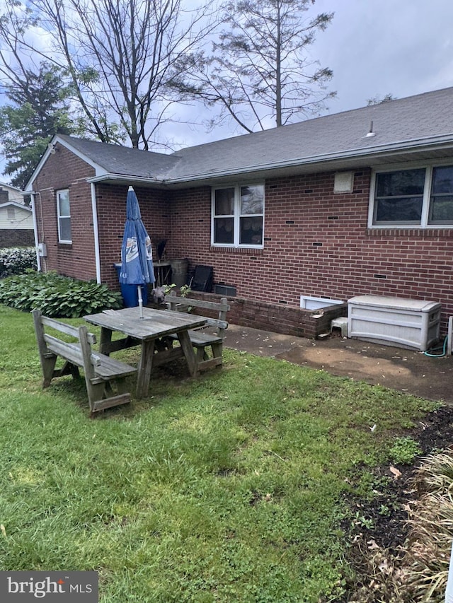 rear view of house with brick siding, a lawn, and a shingled roof