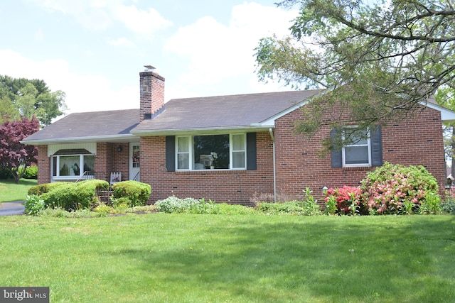 ranch-style house with brick siding, a front yard, a chimney, and roof with shingles