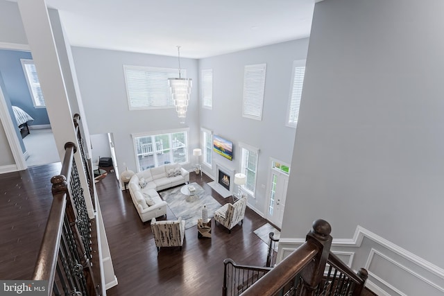 23412 Longollen Woods Ter, Ashburn, VA 20148 - living area with wood finished floors, a chandelier, a towering ceiling, a warm lit fireplace, and baseboards