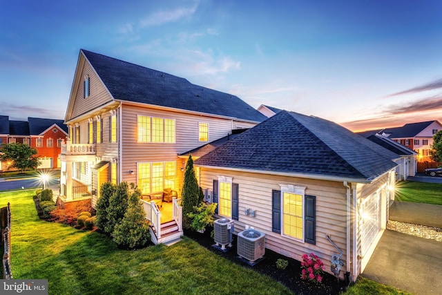 back of house at dusk featuring cooling unit, a yard, and a shingled roof